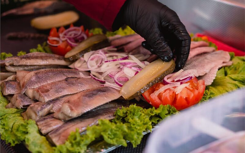 Matjes, Zwiebeln und Tomaten werden von Hand auf einer Platte angerichtet