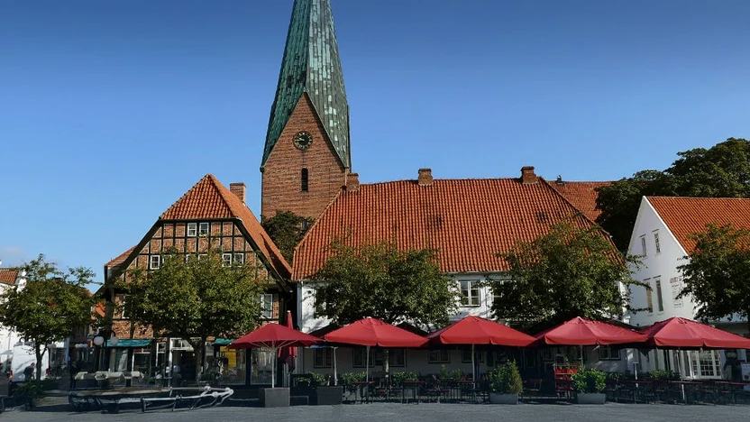 Marktplatz von Eutin mit Kirchturm, Fachwerkhaus und den roten Sonnenschirmen der Marktcafés