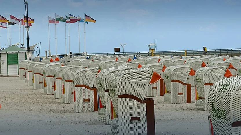 Strandkörbe am Ostseestrand von Grömitz, dahinter die Seebrücke und Fahnenmasten