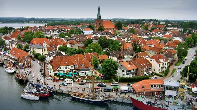 Blick über Neustadt in Holstein: Traditionssegler am Hafen, rote Ziegeldächer der Altstadt und die Stadtkirche